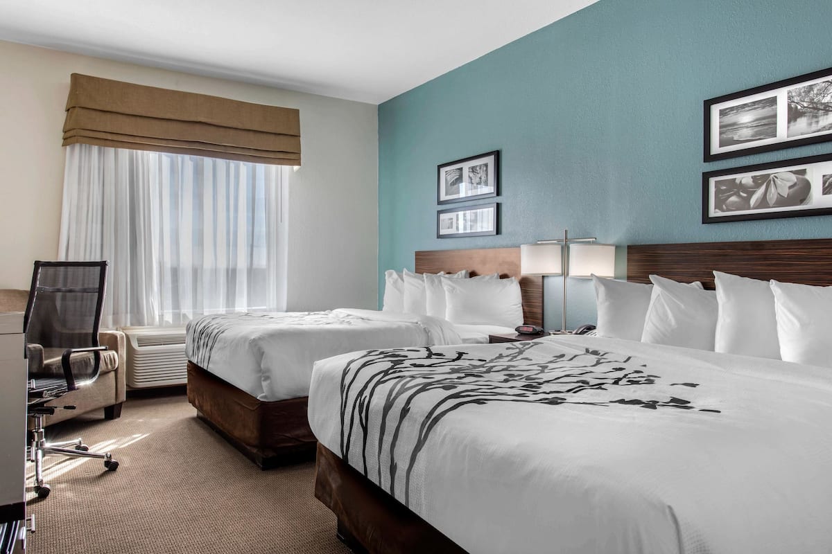 A hotel room with two beds, a desk, a chair, and a window with curtains.