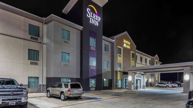 A Sleep Inn hotel with a modern design, featuring a prominent sign, a parking lot with several cars, and a MainStreet Subs restaurant.