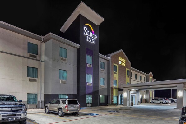 A Sleep Inn hotel with a modern design, featuring a prominent sign, a parking lot with several cars, and a MainStreet Subs restaurant.