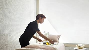 A person attending to a massage table with a towel and a glass bottle, in a room with a tiled wall and a window.