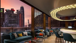 A modern lounge with a city view, featuring sofas, chairs, and a bar area.