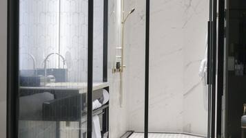 A modern bathroom with a glass shower enclosure, a marble-topped sink, and a glass coffee table with breakfast items.