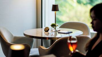 A dining area with a round table, chairs, a lamp, and a view of greenery outside.