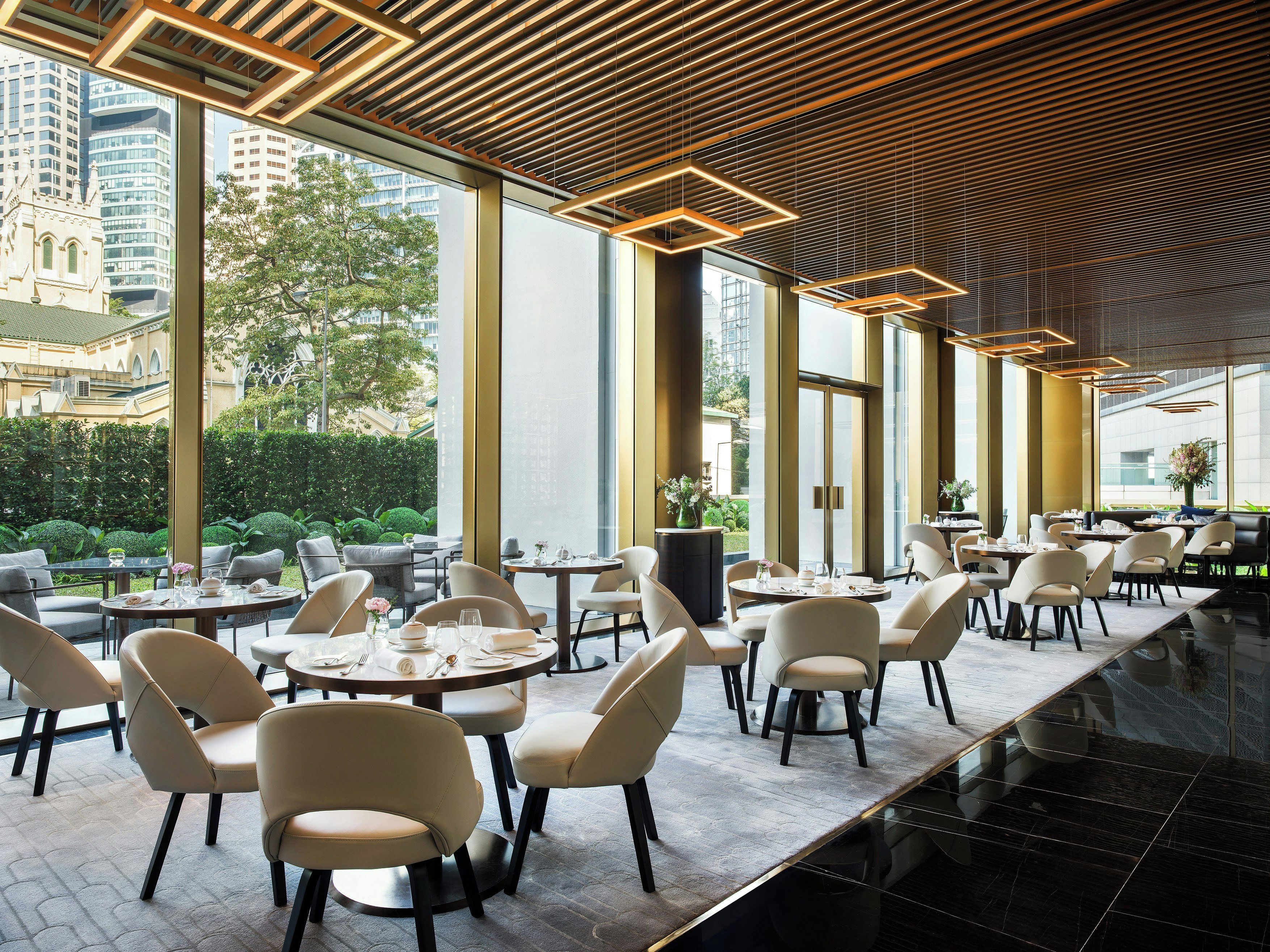 A modern restaurant with round tables and chairs, large windows, and a view of the city.