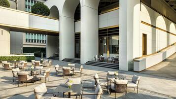 A modern building with a covered outdoor seating area featuring wicker chairs and tables.