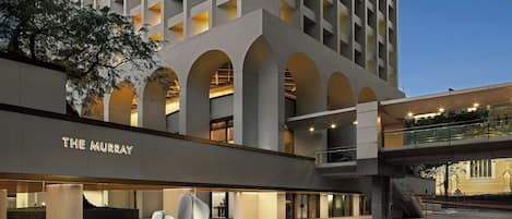 A hotel with a modern architectural design, featuring a prominent entrance with a sign, a covered walkway, and a plaza with sculptural elements.