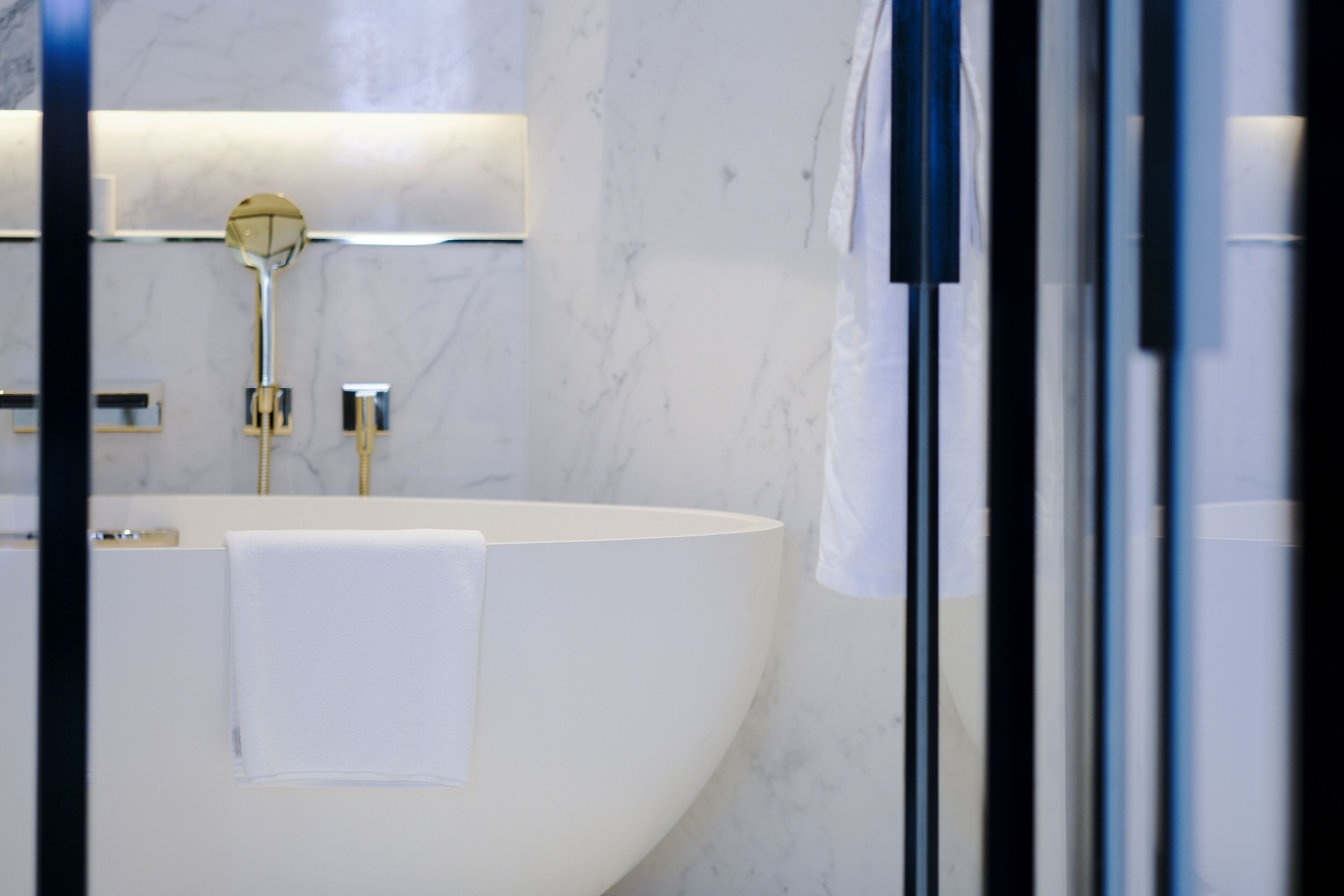 Een moderne badkamer met een groot, ovaal wastafel in het wit, gouden details en een marmeren wand.