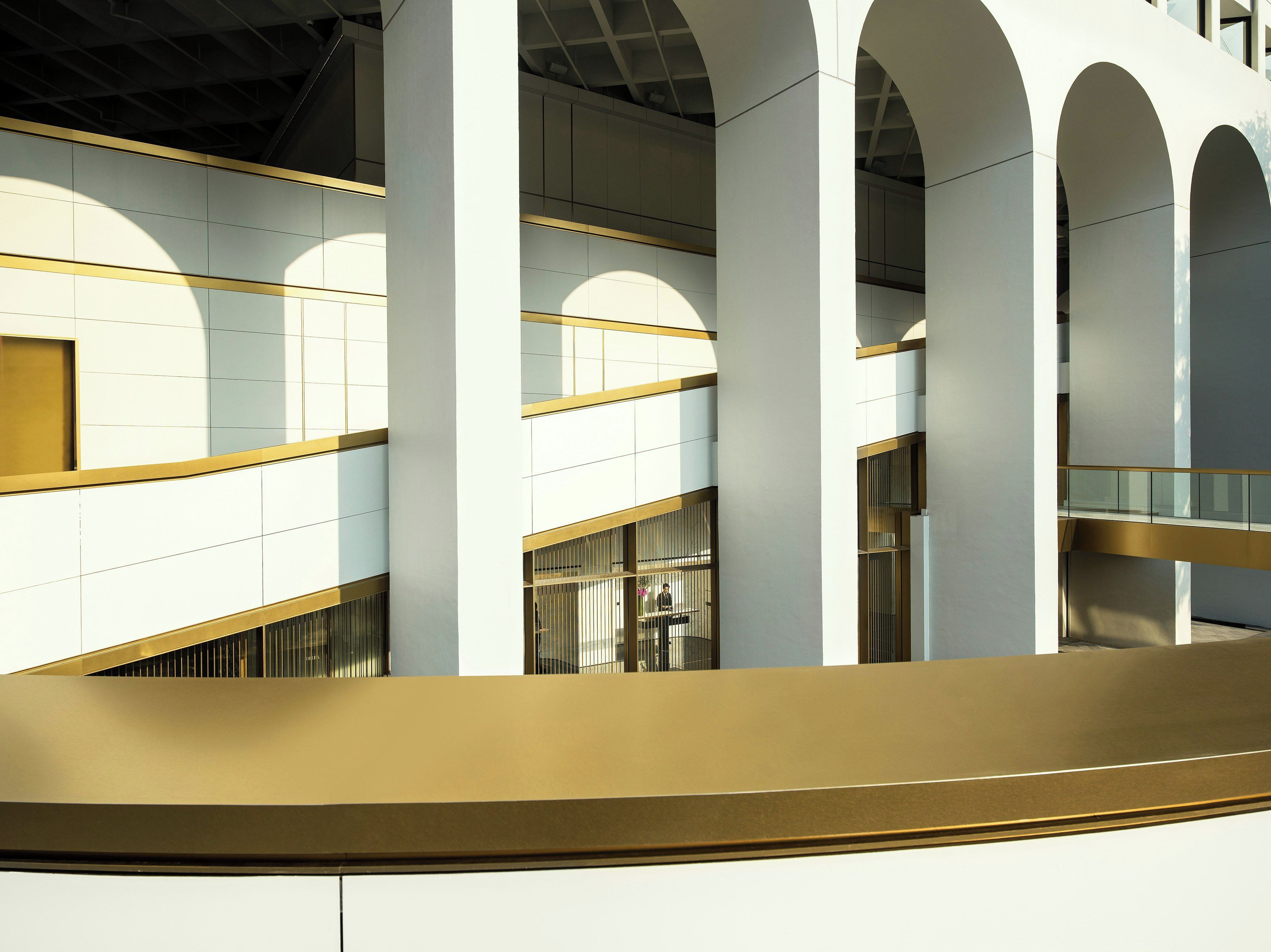 A multi-level interior with white walls and golden accents, featuring a central open space with a curved golden railing.