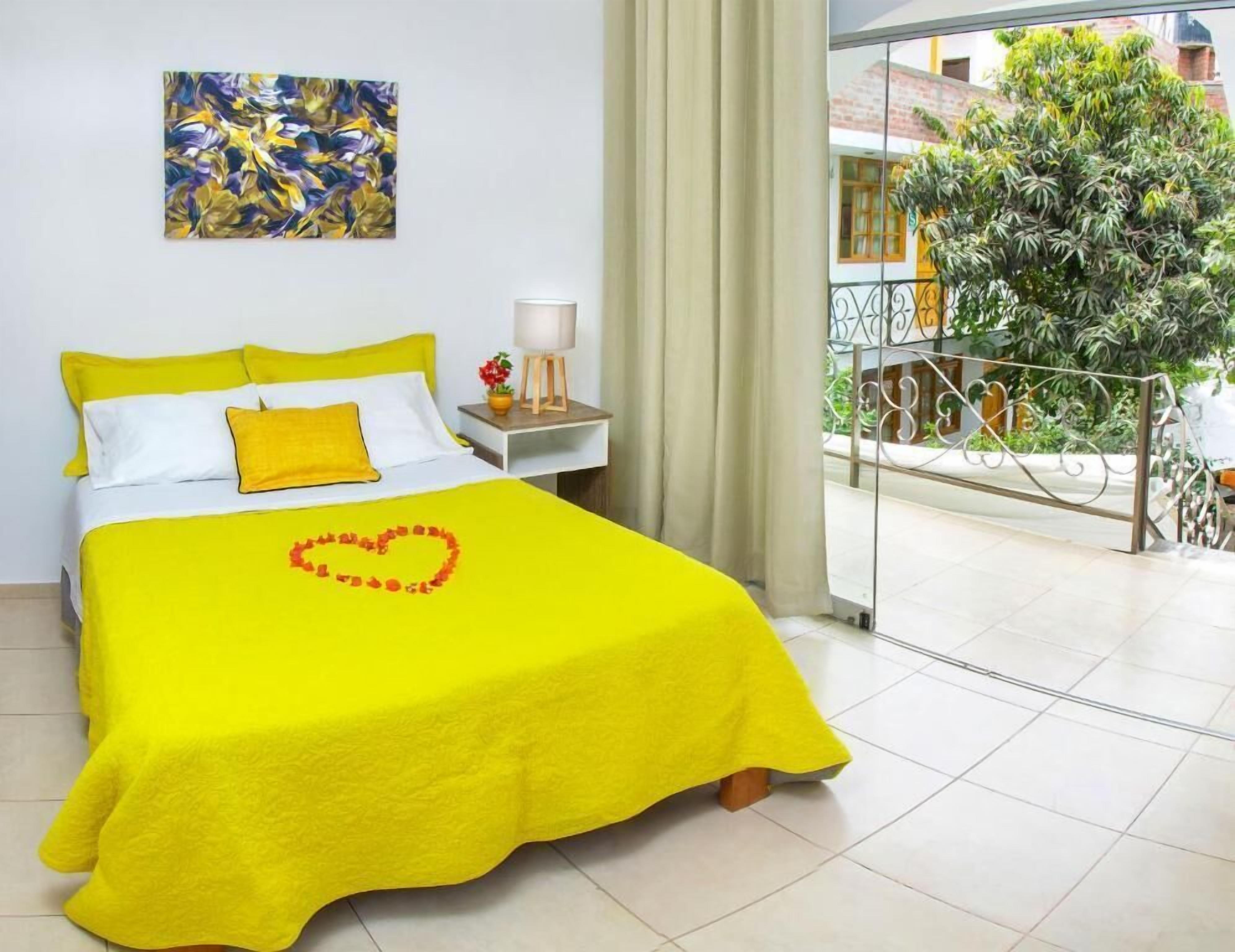 Un llit groc brillant amb una decoració amb forma de cor, un quadre a la paret i un balcó amb vista a vegetació.