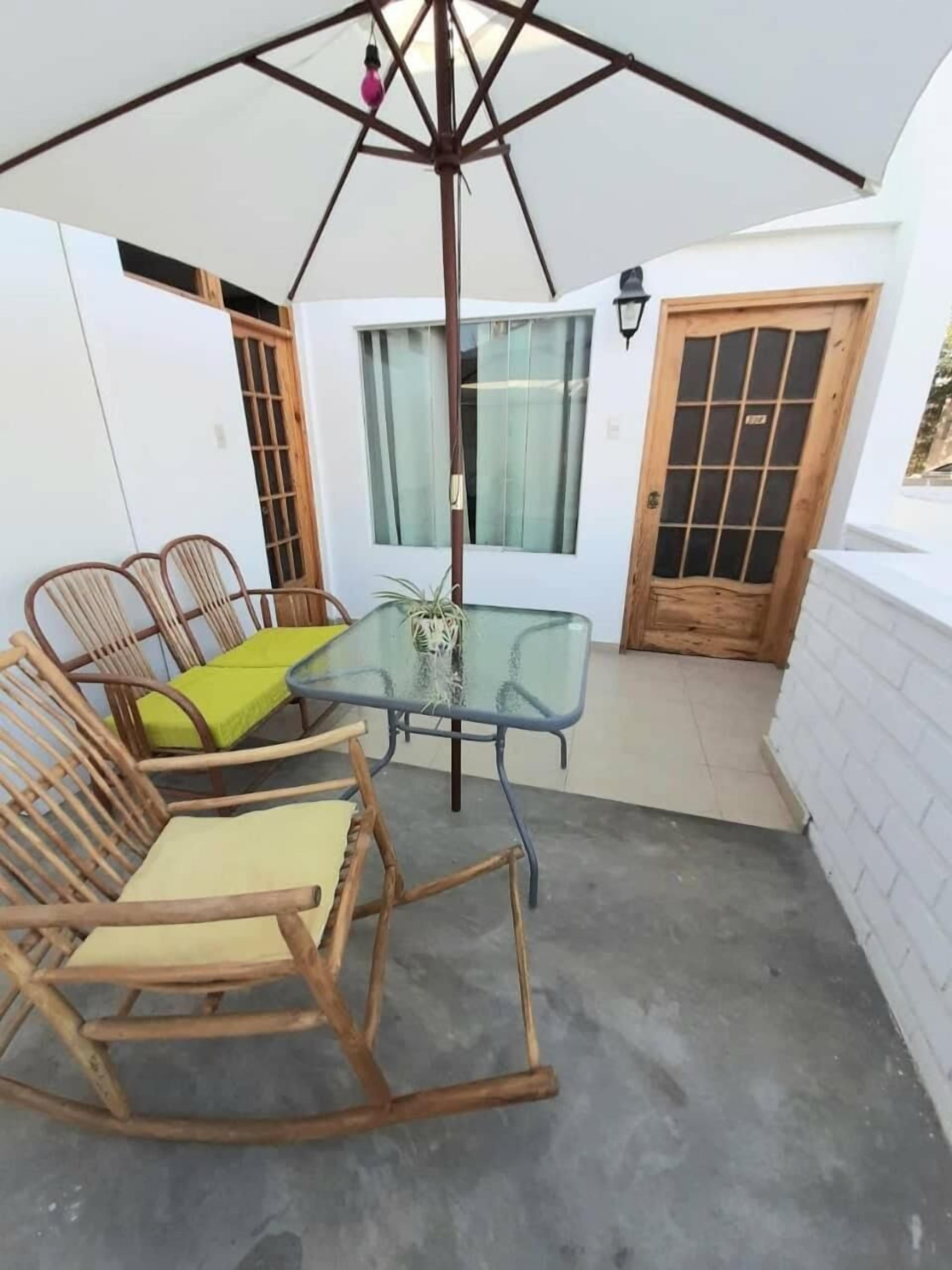 An outdoor patio with a glass table, wicker chairs, a hanging light fixture, and a wooden door.