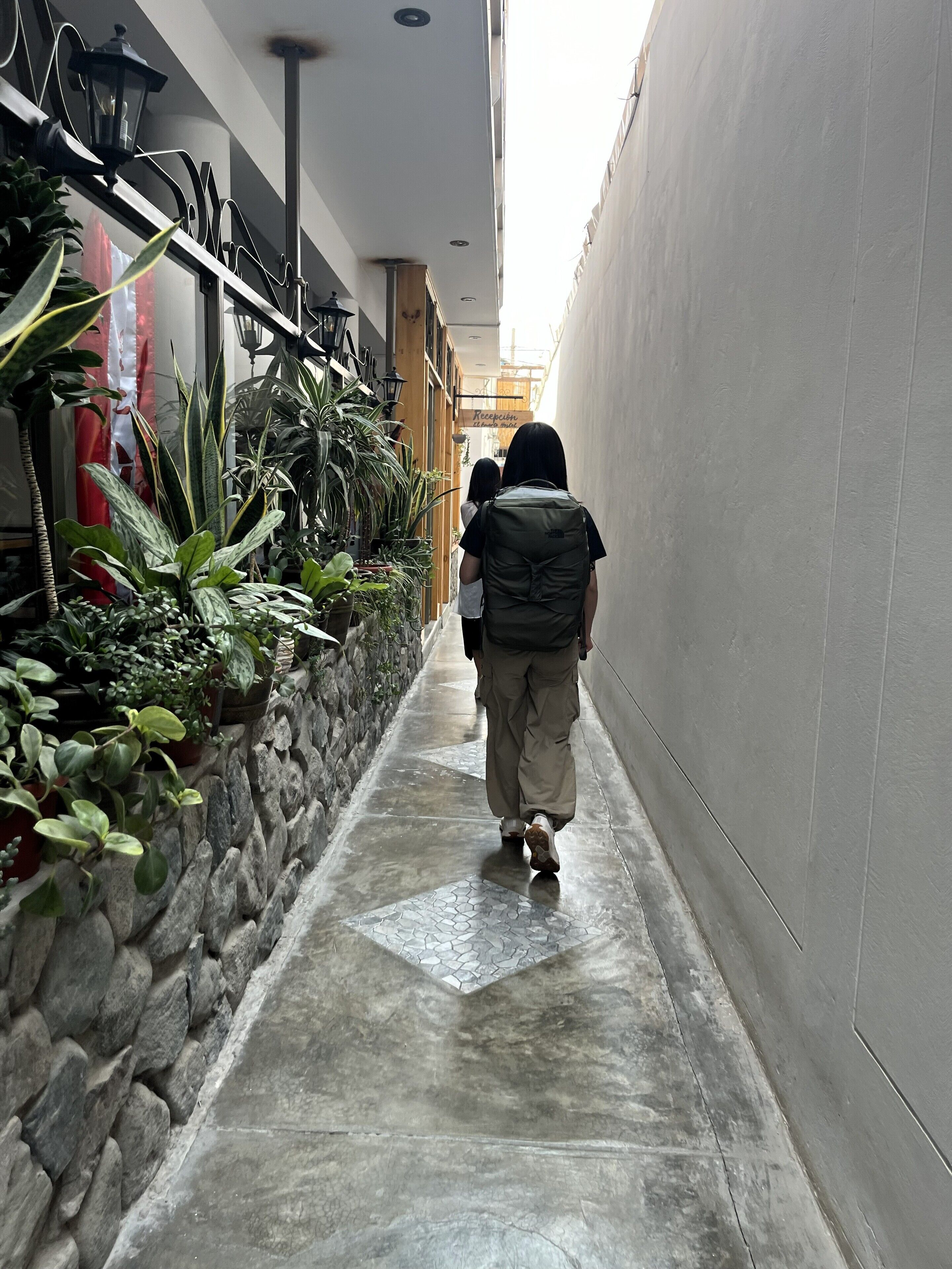 A narrow corridor with a stone wall on one side and a white wall on the other, leading to a reception area.