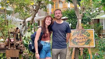 Una pareja de pie en un patio interior con un letrero que dice 'El Huerto Hostel'.