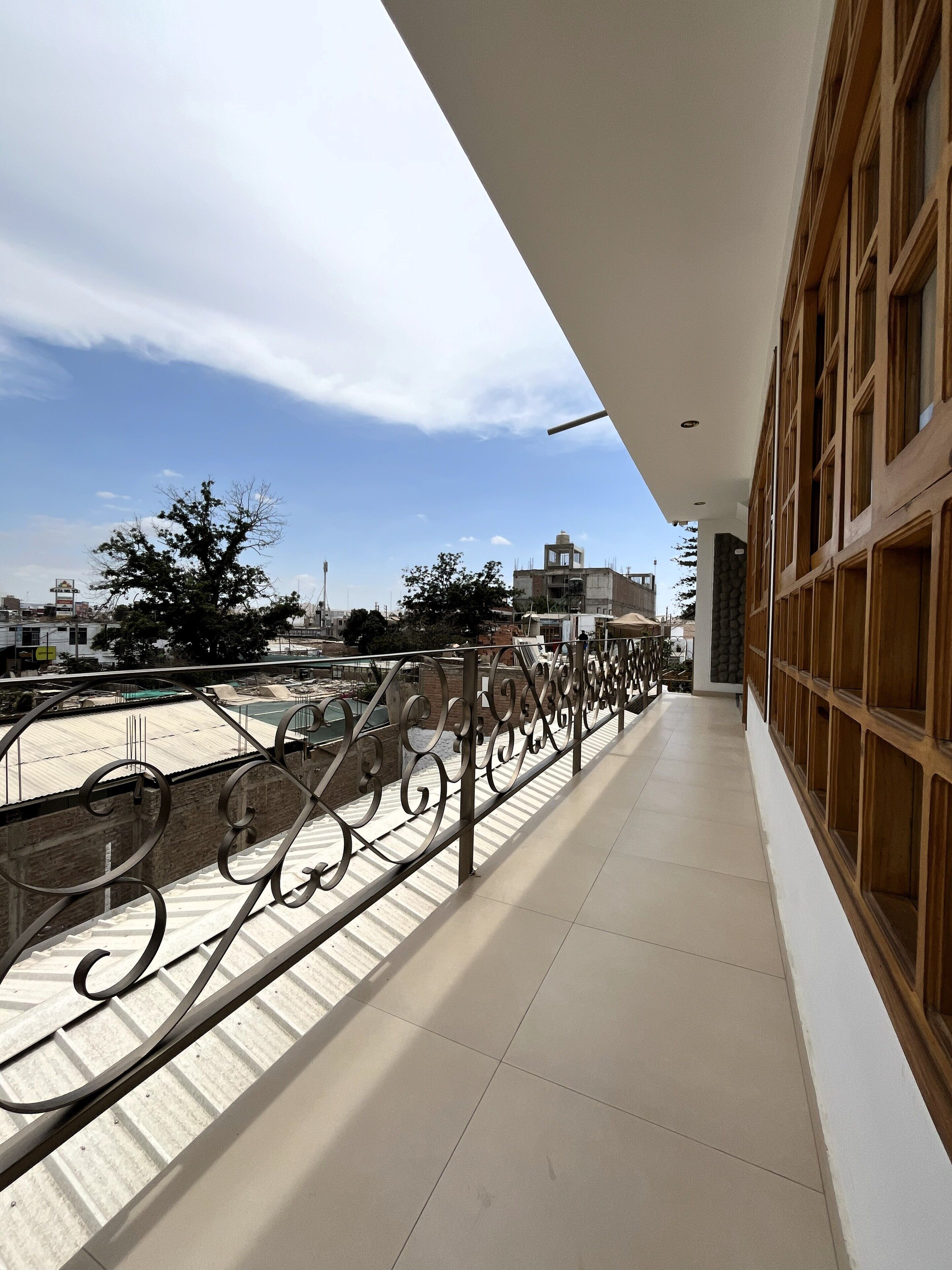 A corridor with a metal railing, leading to a balcony with a view of the cityscape.