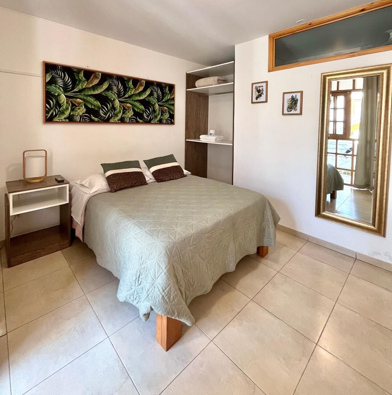 Ein Schlafzimmer mit einem Bett, einem Nachttisch, einem großen Spiegel, einem Kleiderschrank und einem Wandbild.