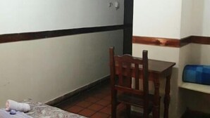 A small room with a bed, a wooden chair, a table, and a blue storage unit. - Prisma Apart Hotel (La Rioja)