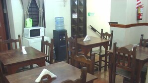 A dining area with wooden tables and chairs, a water dispenser, and a microwave. - Prisma Apart Hotel (La Rioja)