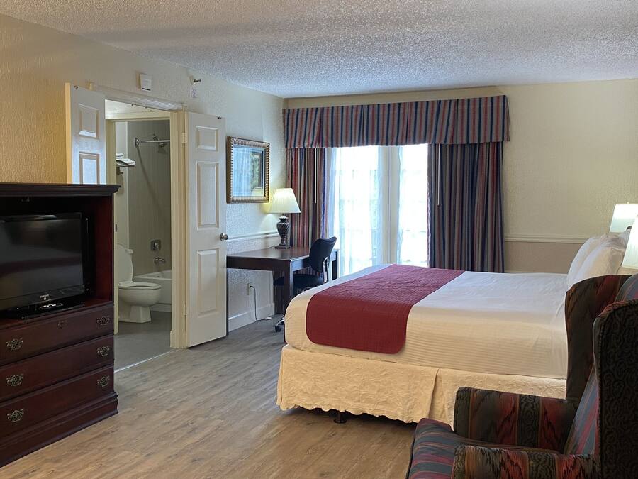 A hotel room with a bed, a TV, a desk, and a bathroom visible through an open door.