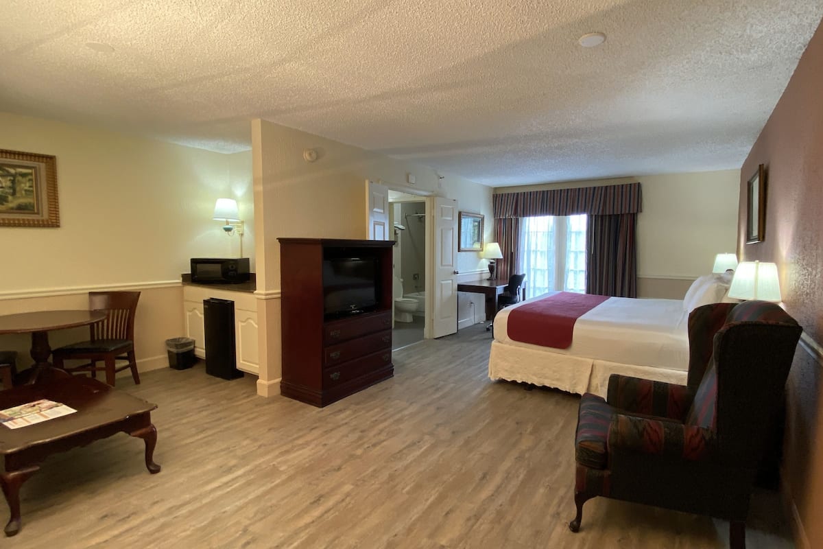 A hotel room with a bed, a desk, a television, a chair, and a bathroom visible through an open door.
