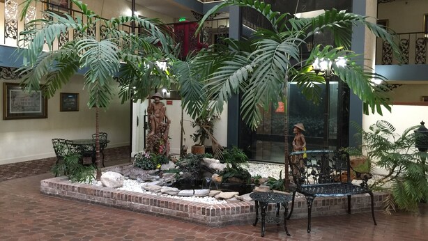 Un vaste atrium intérieur doté d’un jardin central agrémenté de grands pots de plantes, d’une statue et d’une fontaine.