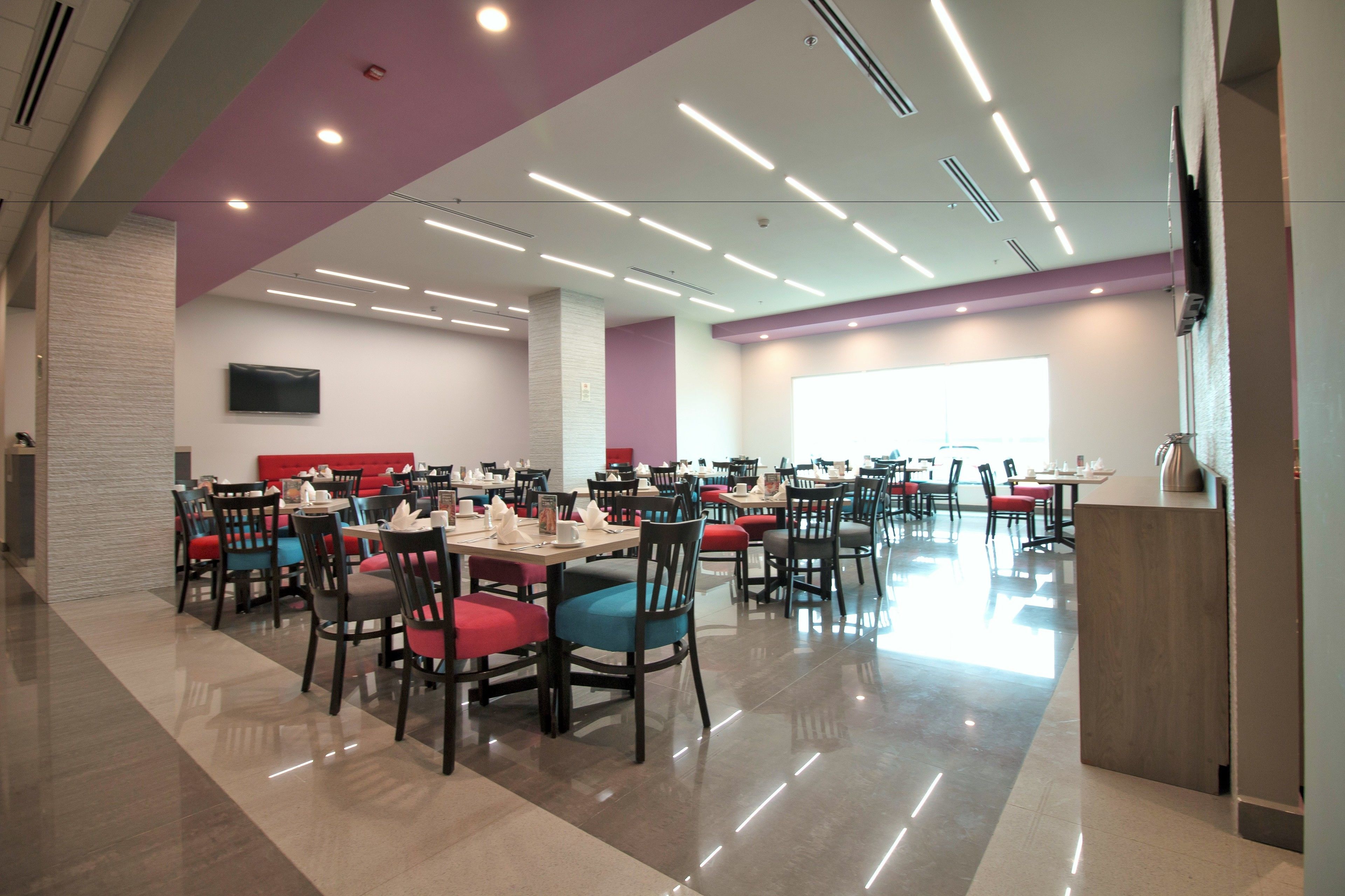Un vaste espace dédié à la salle à manger, avec plusieurs tables et chaises, une grande fenêtre et un téléviseur à écran plat fixé au mur.