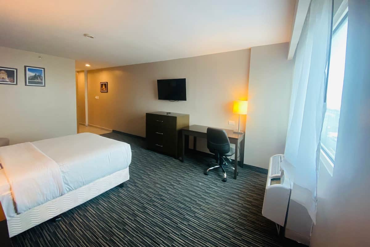 Une chambre d’hôtel avec un lit, un bureau, une chaise, une télévision et une lampe.