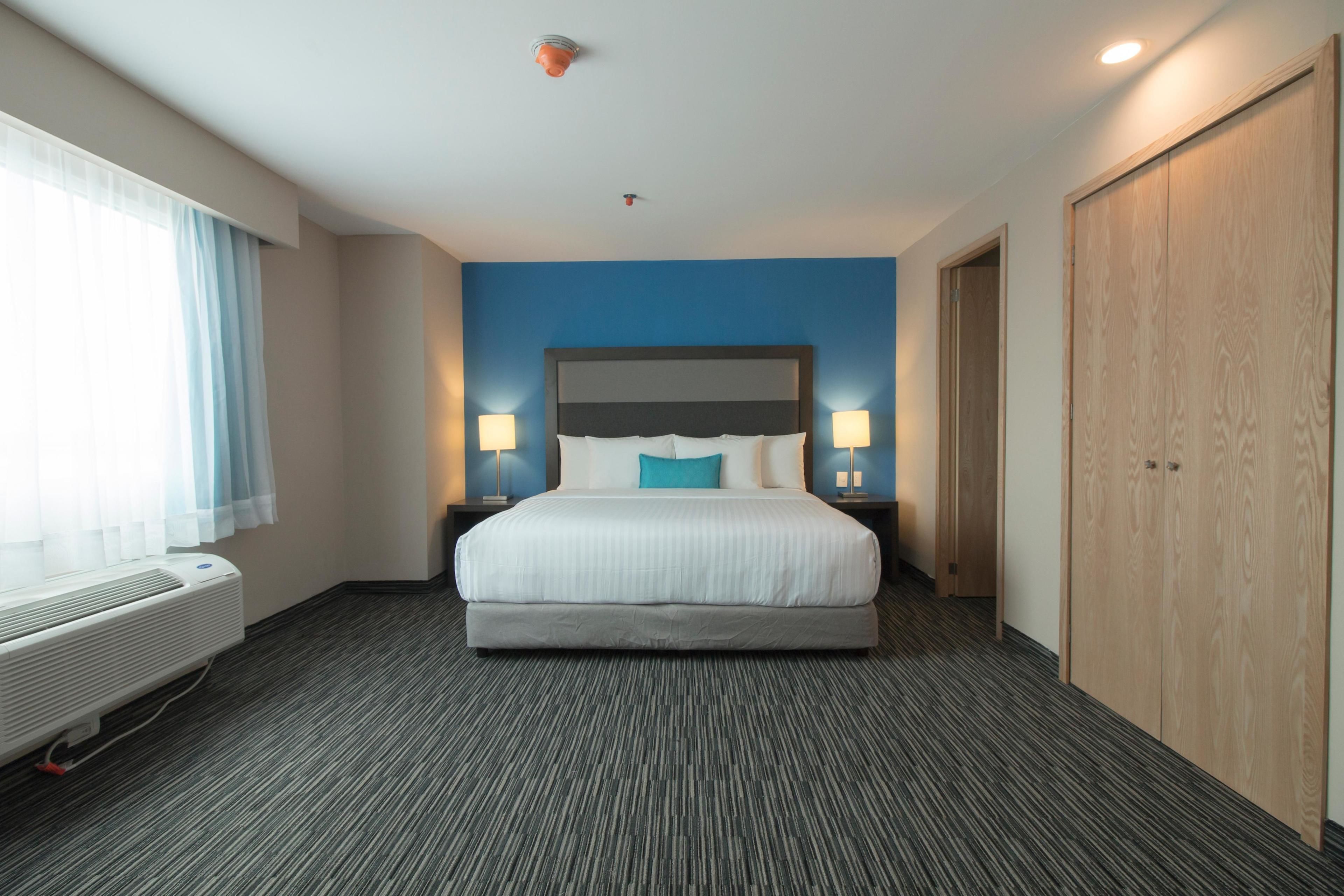 Habitación de hotel con una cama grande, dos lámparas de noche, una ventana con cortinas, un calentador de pared y un armario.