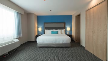 Habitación de hotel con una cama grande, dos lámparas de noche, una ventana con cortinas, un calentador de pared y un armario.