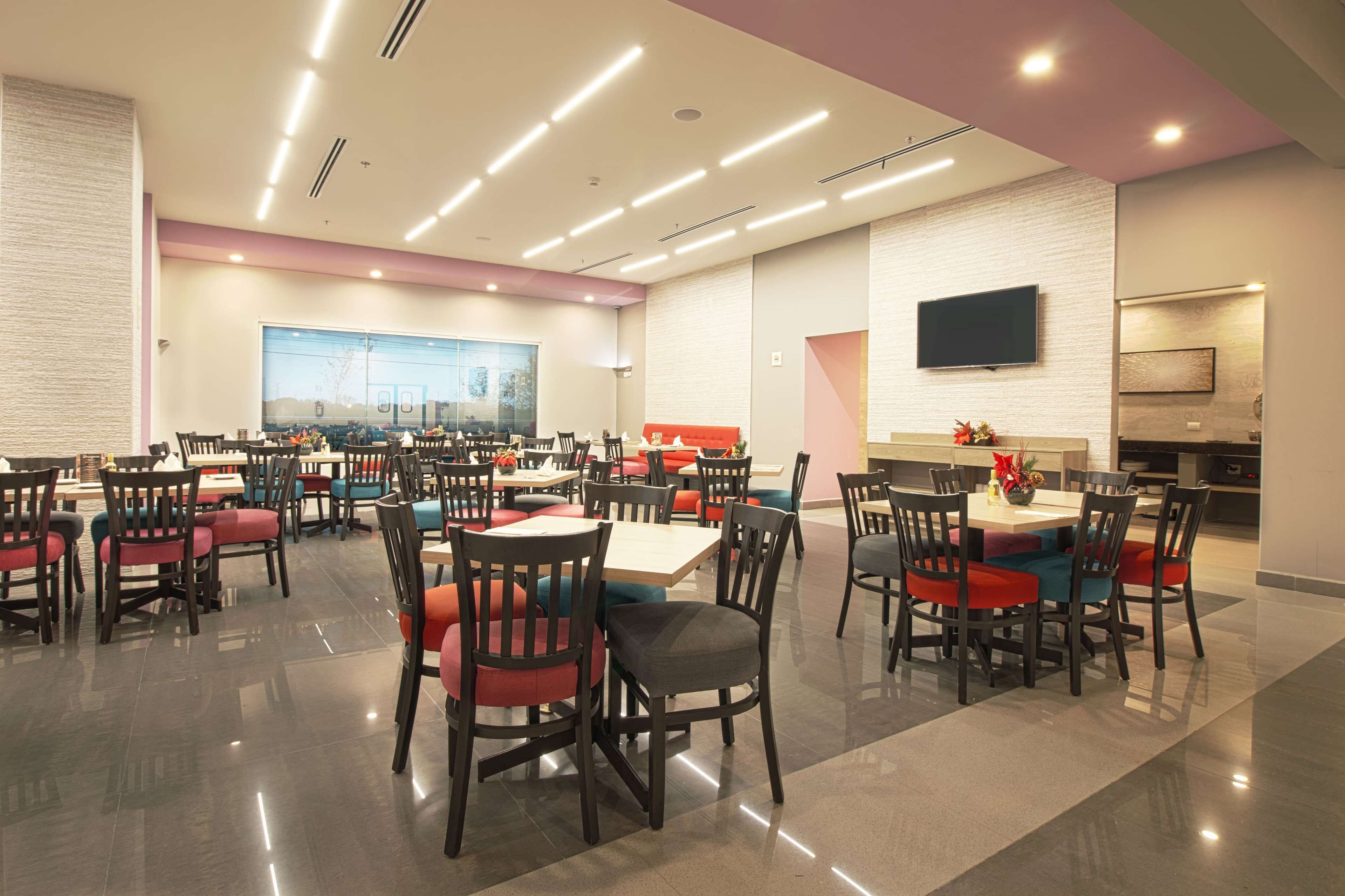A modern dining area with multiple tables and chairs, a large window, and a flat-screen TV mounted on the wall.