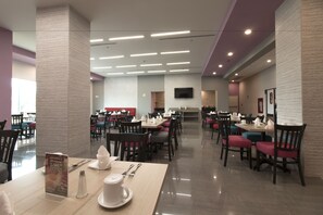 A modern dining area with multiple tables and chairs, a flat-screen TV mounted on the wall, and a clean, well-lit environment.