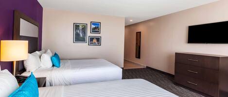 A hotel room with two beds, a TV, a dresser, and framed pictures on the wall.