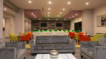 A modern lounge area with a grey sofa, colorful chairs, and a bar with shelves of bottles.