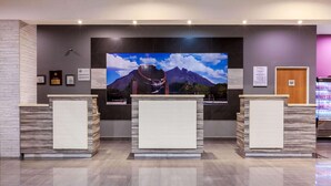 Un espace d’accueil comprenant trois comptoirs de réception, un grand téléviseur mural diffusant des images d’un paysage montagneux et des certificats encadrés accrochés au mur.