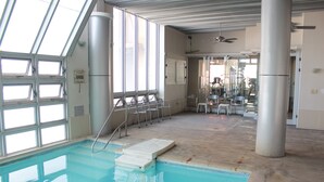 An indoor swimming pool with clear glass walls, a diving board, and a ceiling fan. - Hotel Monterrey Macroplaza (Monterrey)