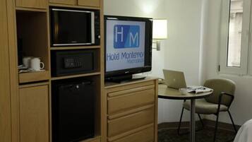Habitación de hotel con minibar, televisión mostrando el nombre del hotel, una computadora portátil y una silla.