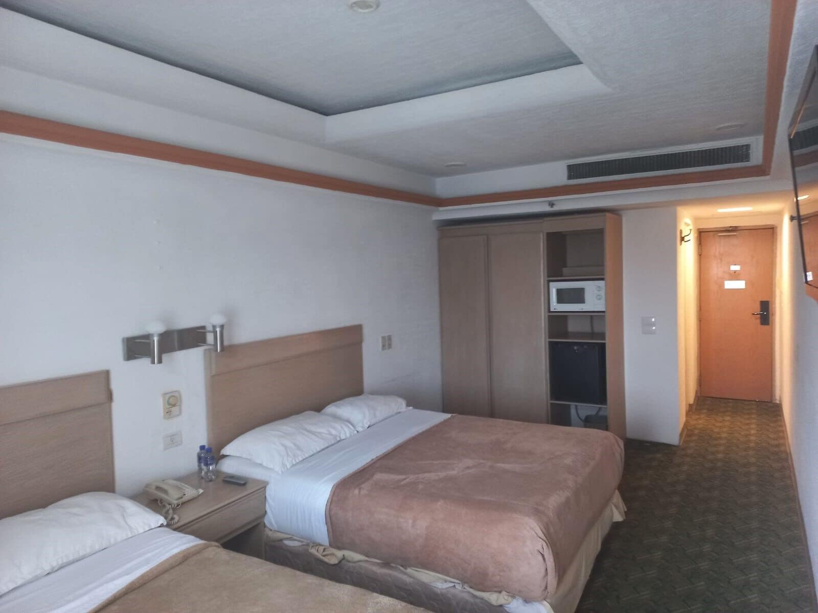 Een hotelkamer met een tweepersoonsbed, nachtkastje met telefoon, magnetron en een kledingkast.