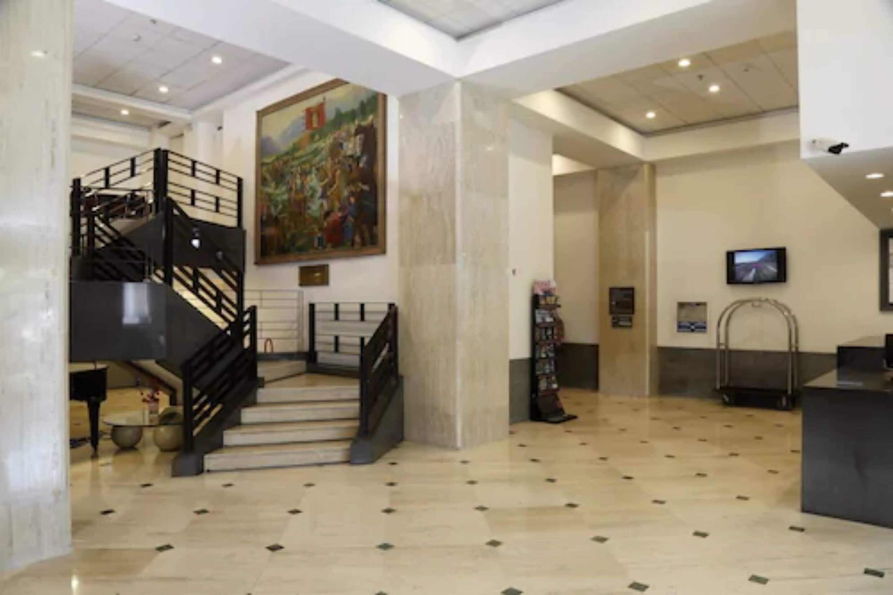 A spacious lobby with a marble floor, a staircase with black railings, a large painting on the wall, and a reception desk.