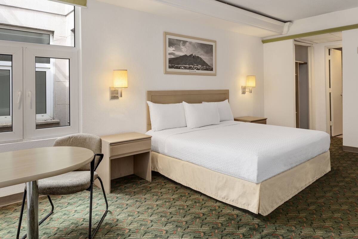 A hotel room with a bed, bedside tables, a chair, a desk, and a window.