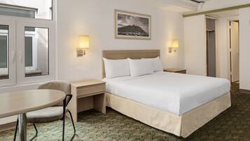 Quarto de hotel com cama, mesas de cabeceira, uma cadeira, escrivaninha e janela.