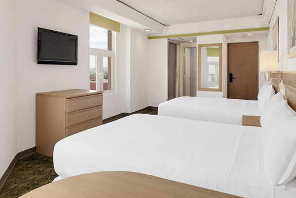 Une chambre d’hôtel avec deux lits, un téléviseur fixé au mur, une commode et une fenêtre donnant sur un beau paysage.