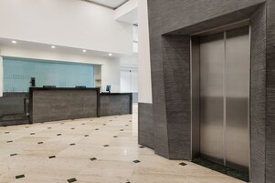 Un área de recepción moderna con un mostrador de registro, una recepción y un ascensor.