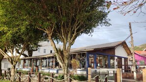 A restaurant with outdoor seating, a large tree, and a fence. - Pousada Marinamarela (Penha)