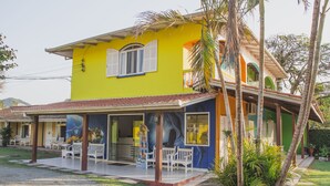 A yellow building with a covered porch, white benches, and palm trees. - Pousada Marinamarela (Penha)