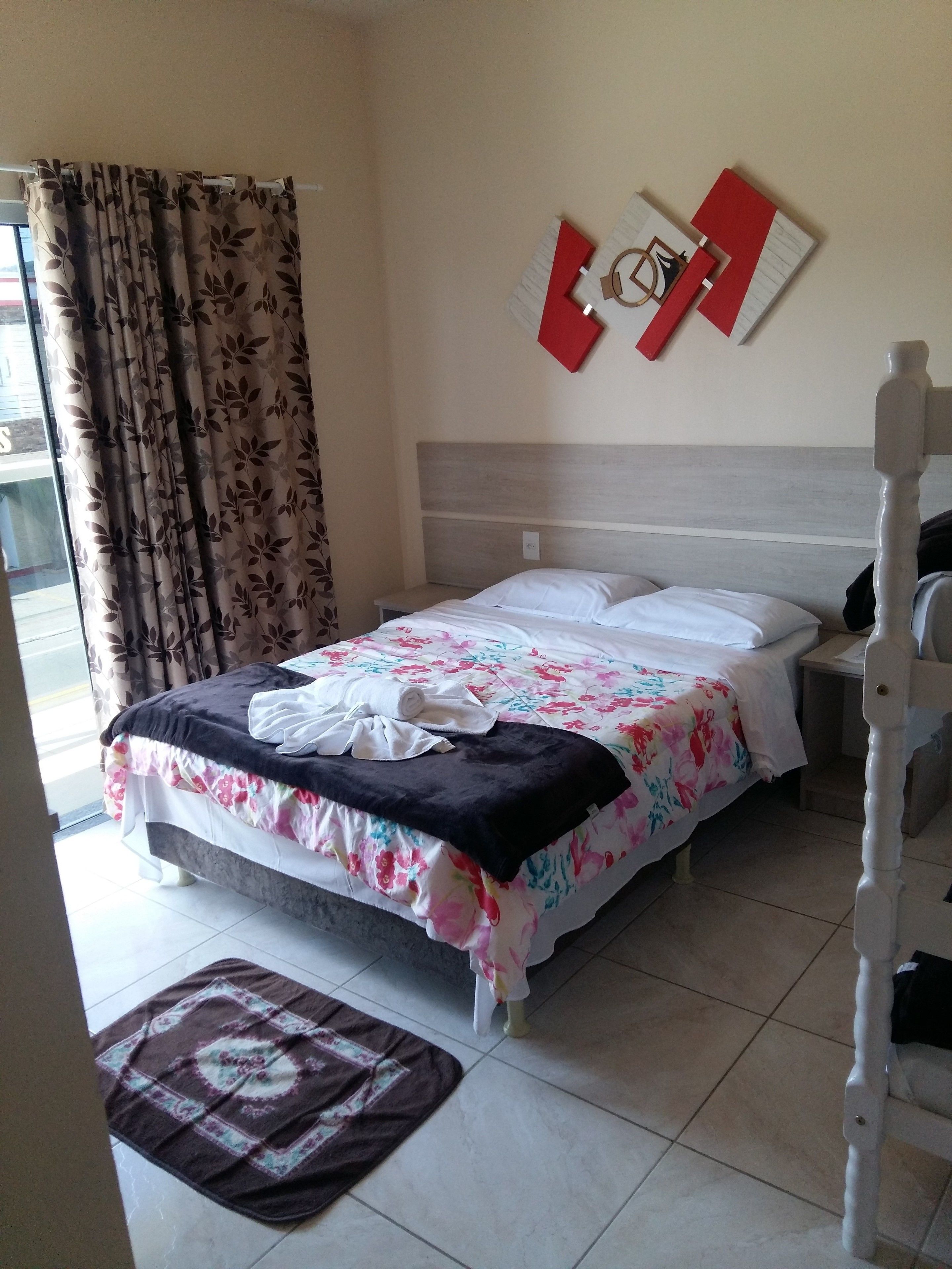 Una cama bien hecha con ropa de cama floral, un cabecero de madera y un adorno de pared rojo y blanco.