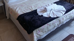 A neatly made bed with a floral comforter, a dark blanket, and rolled towels. - Hotel Rochamar (Penha)