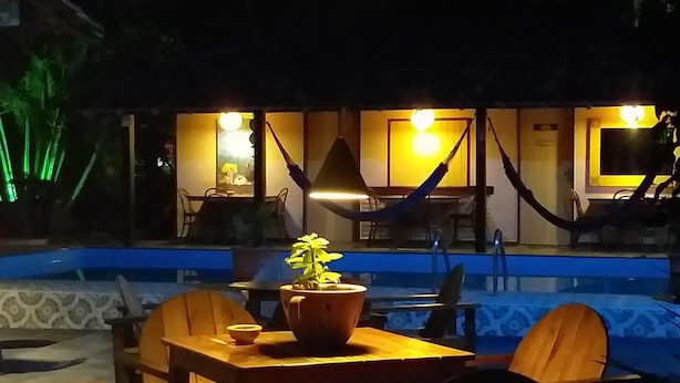 Área de piscina com mesa, cadeiras e uma rede.
