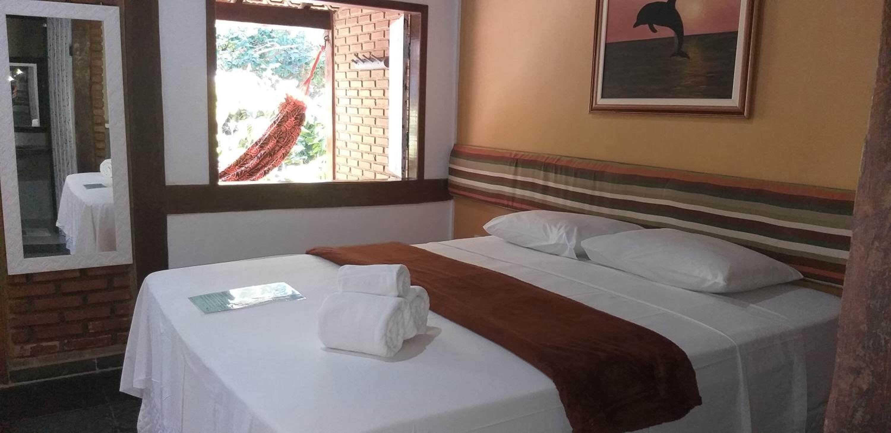 Ein Hotelzimmer mit Bett, Fenster mit Blick auf Grünflächen, einem Bild an der Wand und einem gestreiften Kopfteil.