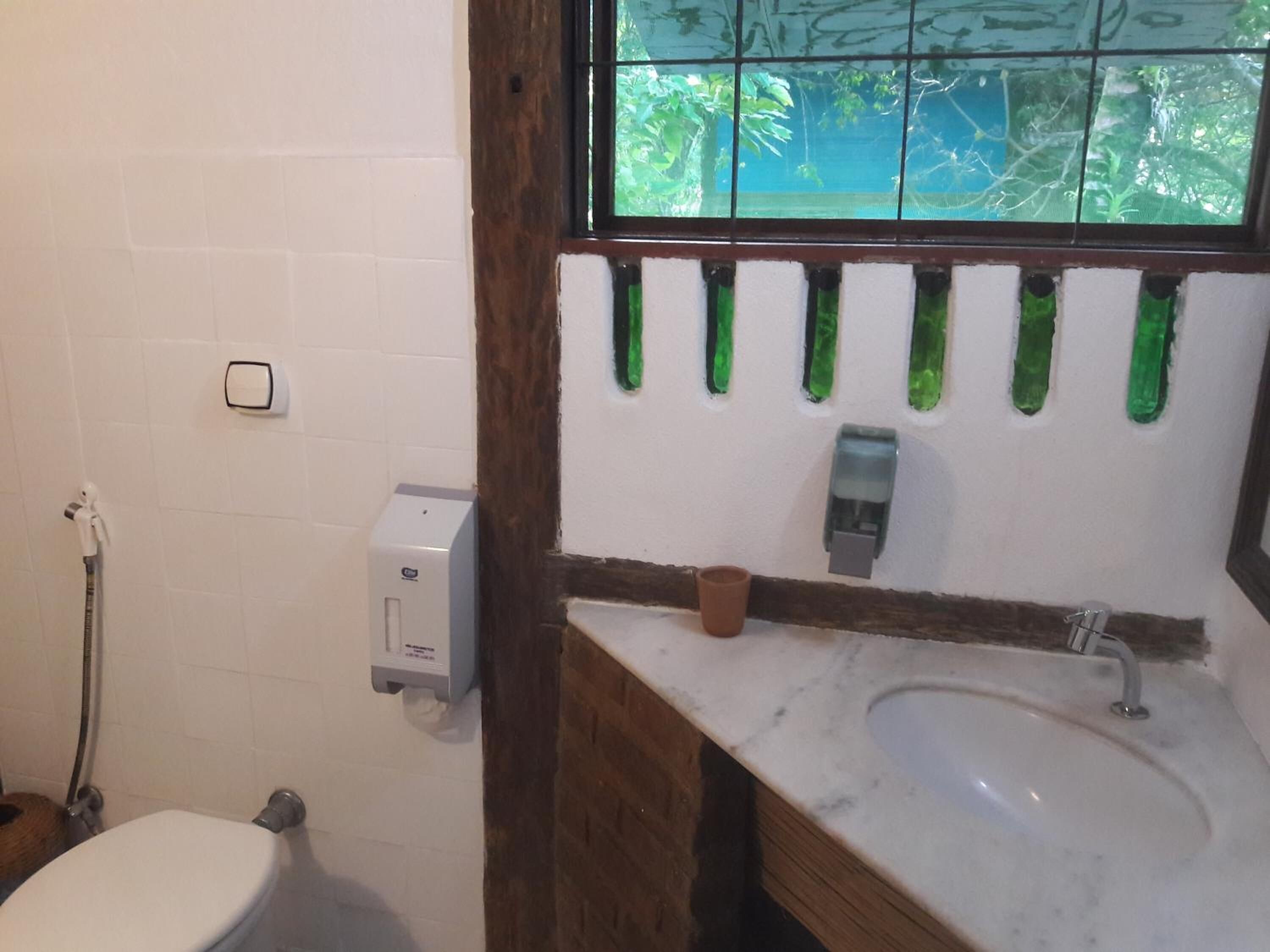 A bathroom with a white toilet, a sink with a marble countertop, a window with green glass panes, and a hand dryer.