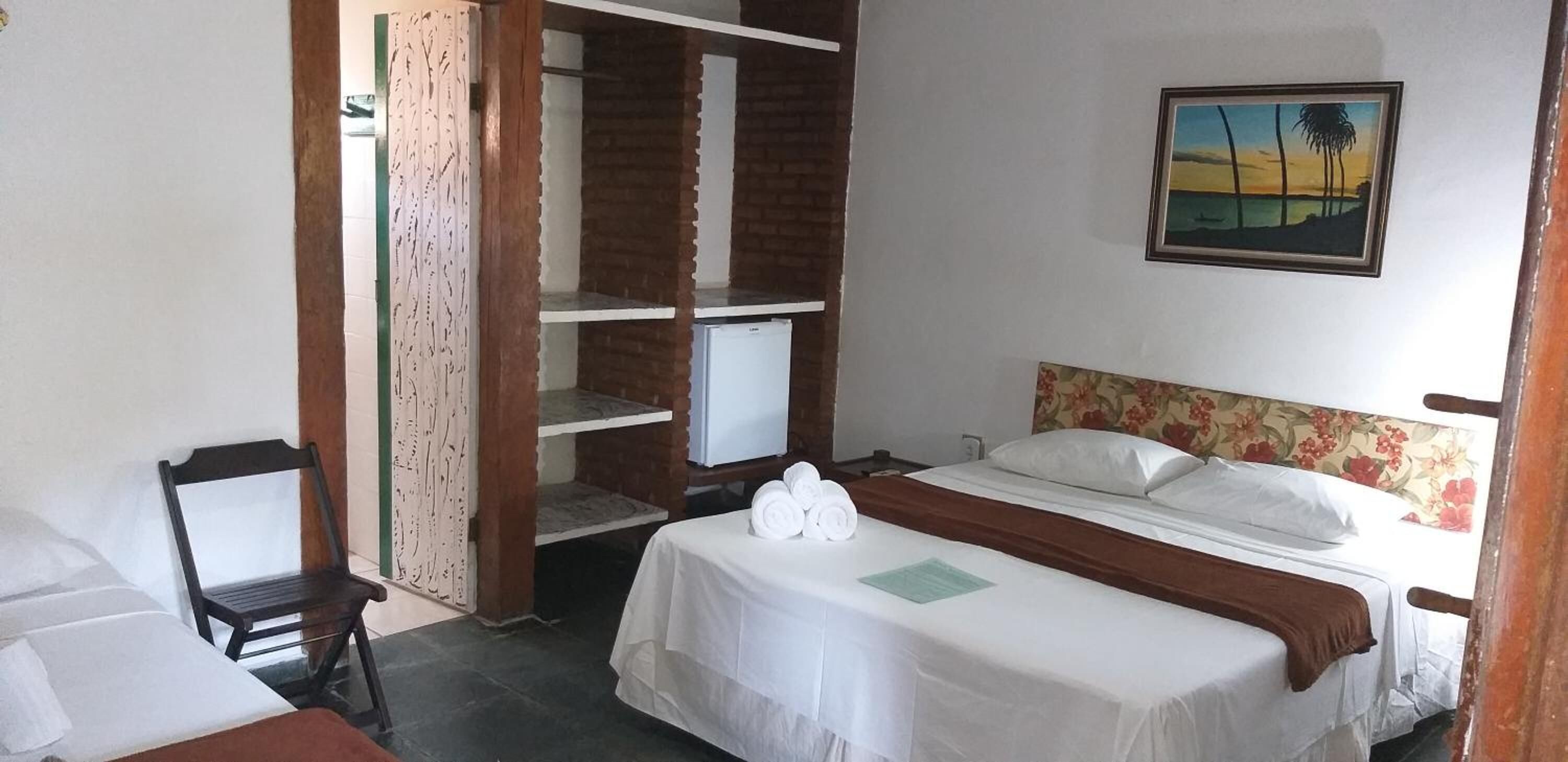 Een hotelkamer met een bed, een stoel, een kledingkast en een schilderij aan de muur.