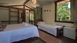Quarto com duas camas de solteiro, uma pequena escrivaninha, janela com vista para o verde e luminária no teto.