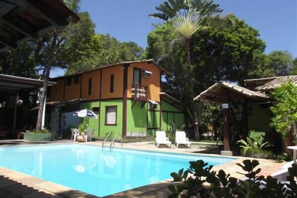 Una piscina con sillas de descanso y un edificio de fachada verde y naranja.